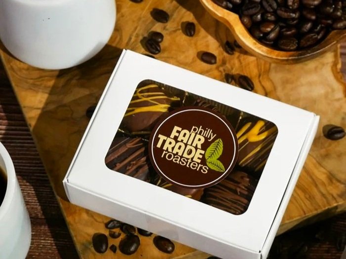 A box of espresso and peanut butter truffles on a wooden board with coffee beans littered around